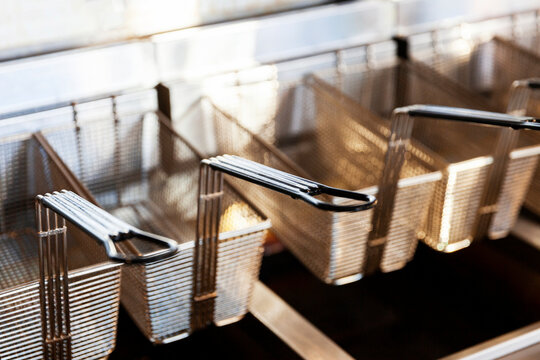 Stainless steel deep fryer wire baskets hanging on shelf.