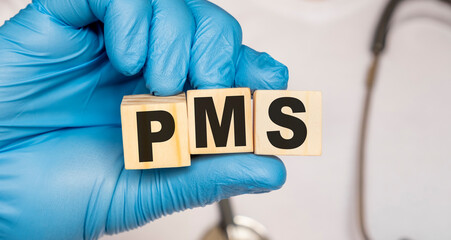 PMS Premenstrual syndrome - word from wooden blocks with letters holding by a doctor's hands in...