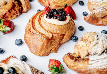 Delicious role of cheesecake croissant dough with blackberries and strawberries on top on a white table and flavored roles around.