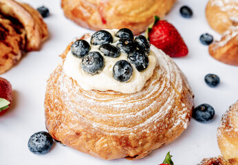 Exquisite lemon pie croissant dough role with blackberries on top on a white table and flavored roles around it.