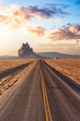 View of a road in a dry desert with a Shiprock mountain peak in the background. Sunrise Sky Art...