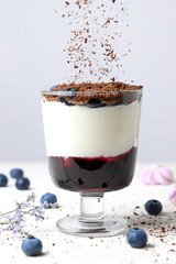 Creamy dessert with blueberries and grated chocolate in a glass on a white table