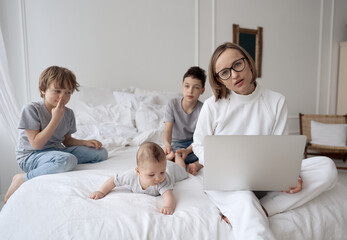 Busy caucasian woman trying to work while baby sitting three kids. Caucasian single mom work from home with the children. High quality photo