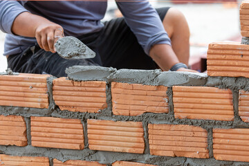 A close up of orange bricks with the hands of a mason We are building the walls of the house, designing the arrangement of bricks to create the walls