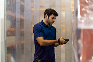 Male warehouse worker using barcode machine checking products or parcel goods on shelf pallet in...