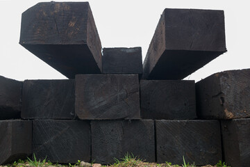 View of the end parts of the stacked rows of black tarred old rectangular railway sleepers lying on the ground with fine grass, a look of perspective.