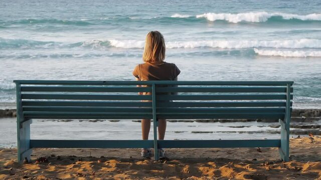 Woman enjoying ocean view from a bench at sunset. Back view.