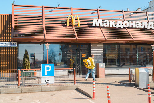 Facade Of A McDonald's Family Fast Food Restaurant Outside During The Day. A Yandex Food Delivery Man Is Standing Nearby. Smolensk, Russia 04.12.2021