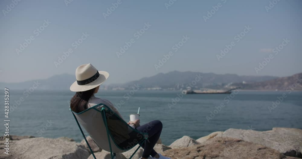 Poster woman sit at outdoor and enjoy the sea with her drink