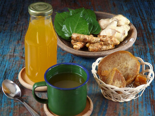 Jamu or Indonesian traditional herbal drink made from turmeric, ginger, betel leaves, tamarind, palm sugar. Healthy drink with mixed sour, sweet, and spicy taste. Ingredients in background