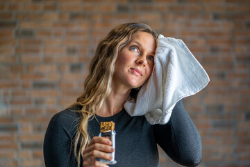 Beautiful fitness woman with a towel eating a protein bar after working out at the gym. Sporty...