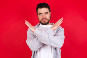 young handsome caucasian man in sports clothes against red wall Has rejection angry expression on face and crossing hands doing refusal negative sign.