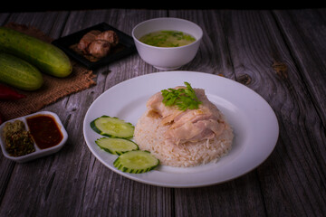 Hainanese chicken rice or Khao Man Gai Asian food in a wood white plate with delicious broth and dipping sauce.