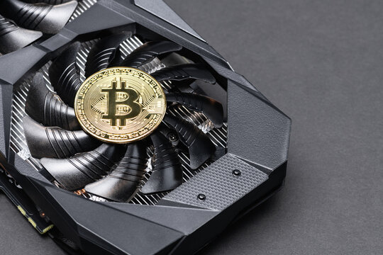 Gold Bitcoin coin on a Black video Card on a gray background. Crypto currency, close up. Bitcoin mining concept