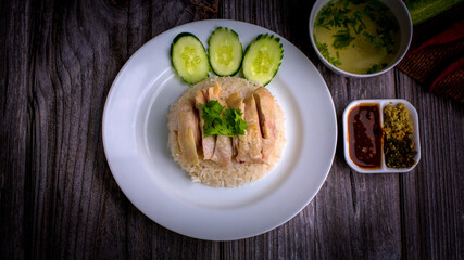 Hainanese chicken rice or Khao Man Gai Asian food in a wood white plate with delicious broth and dipping sauce.