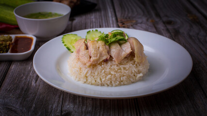 Hainanese chicken rice or Khao Man Gai Asian food in a wood white plate with delicious broth and dipping sauce.