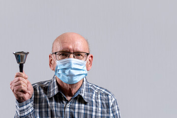 Old bald man with glasses and medical mask with bell in his hand. Copy space.