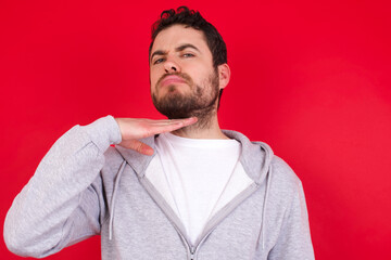 young handsome caucasian man in sports clothes against red background cutting throat with hand as knife, threaten aggression with furious violence.