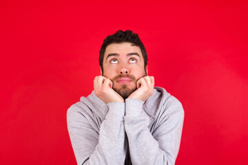 Portrait of sad young handsome caucasian man in sports clothes against red background hands face look empty space