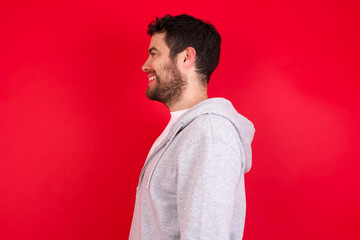 Profile portrait of nice young handsome caucasian man in sports clothes against red background look empty space toothy smile