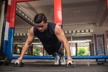 A fit asian man does wide push ups with push-up bars at a MMA gym. Body weight calisthenics or HIIT...