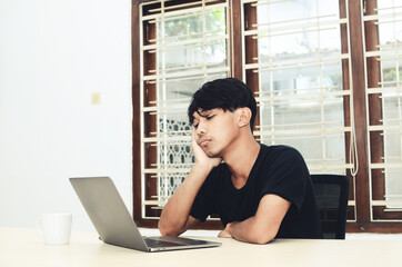 The man in black Asian t-shirt sat in front of the laptop with a disappointed expression