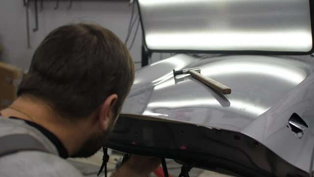 Middle aged man - professional repair worker uses modern technology in demand removing dents from a metal car surfaces with no painting needed. Minor damaged car surfaces modern way to repair clever