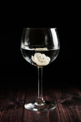 A flower submerged in a dark background, clear wine glass.
