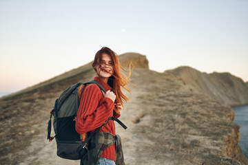 woman tourist climbs to the top of the bar along the road with a backpack on her back