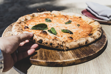 Woman hand taking slice of vegetarian pizza fresh from the pizza oven. Italian cuisine.