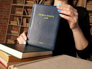 Attorney holds HUMAN RIGHTS LAW book. Human rights law prescribes obligations which states are...