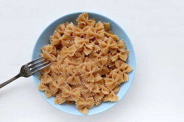Wholegrain farfalle pasta in a bowl on white table background. Healthy vegetarian food. Top view, copy space