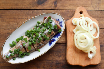 Pieces of salted herring fish on a plate withgreen onion and  onion rings. Swedish pickled herring on wooden table background. Midsummer traditional food. Top view, copy space	