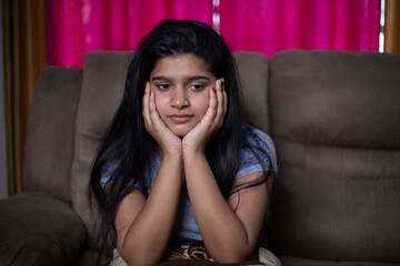 Obraz premium Alone sad young girl thinking about problems while sitting on sofa - concept of negative emotions, mental health illness due to coronavirus covid-19 pandemic.