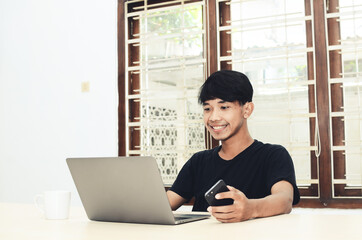 The Asian man is sitting in front of the laptop with a happy expression