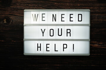 We Need Your Help word text in light box on wooden background