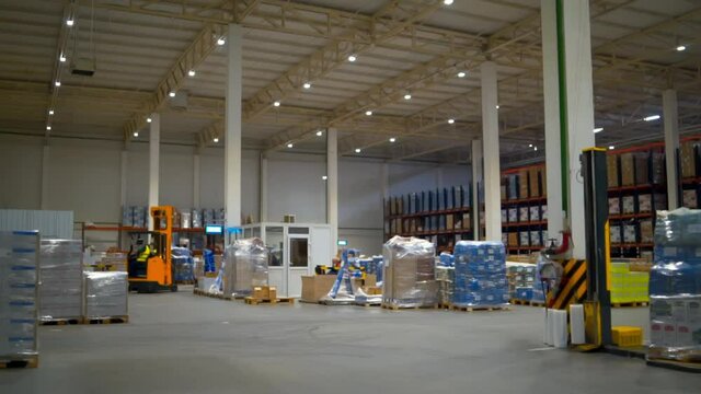 A big warehouse with a lot of good with moving forklift inside. Static shot of working process.