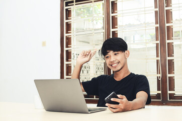 An Asian man is sitting in front of the laptop with a smiling expression