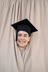 Education, graduation and people concept - happy male student coming out of beige curtains. Funny cheerful face. People emotions