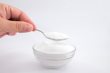 female hand holds a spoon with soda. baking soda in a glass bowl and spoon on a white background.