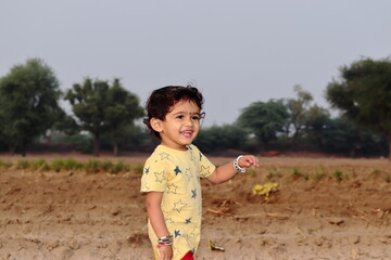 low angle  close-up portrait of  An Indian child stands in the field looking at the camera