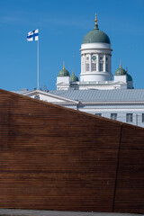 The dome of Helsinki lutheran cathedral behind a wooden wall. Finnish flag waiving in the foreground.