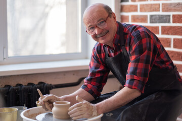 Senior male potter creating bowl in pottery workshop. - obrazy, fototapety, plakaty
