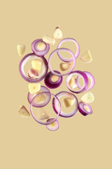 flying onion rings and sliced garlic cloves isolated on a beige background.