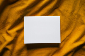 Blank white card on yellow fabric background. Elegant feminine composition. Empty space for text. Copy space. 