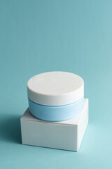 Face cream jar with plastic cap and whire carton box, package on blue background. Mockup unbranded cosmetology product