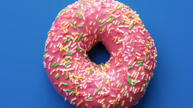 Rotation fresh ring donut with pink glaze isolated on blue top view. Close up shot on 4k RED camera
