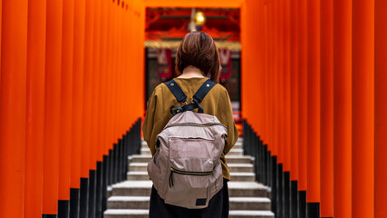 Fototapeta na wymiar Ikuta Shrine (Kobe, Sannomiya), Row of torii, young Asian woman traveler with a backpack, Japan travel, gorgeous, architecture, Tourist attraction, God of love place, red gate, Worship god Fox.