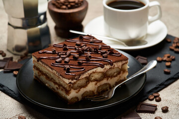 Portion of Traditional Italian Tiramisu dessert and mocha coffee maker on grey concrete background