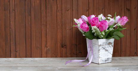 Blumenvase mit Tulpen und Rosen vor Holzhintergrund.